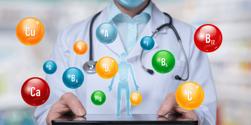 Person in a lab coat holding a tablet with floating vitamin and mineral symbols.