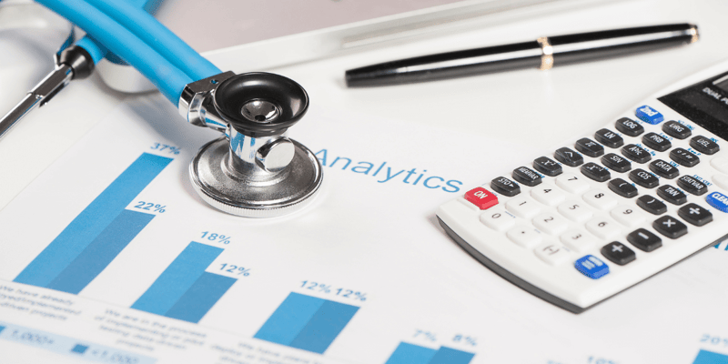 Stethoscope, calculator, and pen on a desk with bar charts and the word 